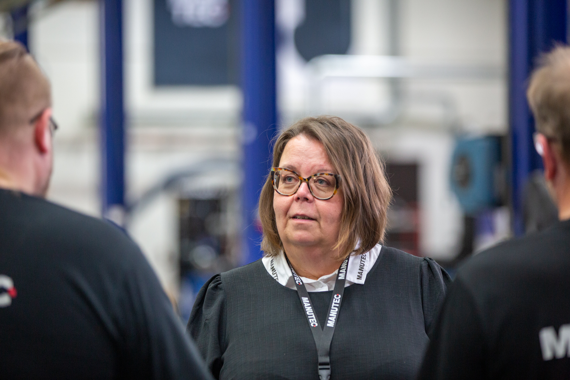 Manutecin toimitusjohtaja Kirsi Junnilainen keskustelee kahden henkilön kanssa Manutecin tuotantotiloissa. Henkilöt näkyvät etualalla selkäpuolelta rajattuina.